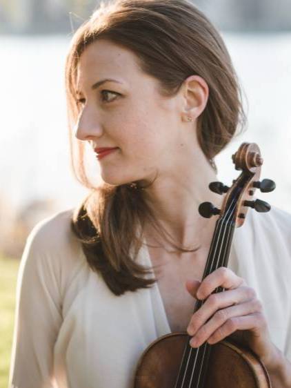 a women in a white top holds a violin in front of an unfocused outdoor background