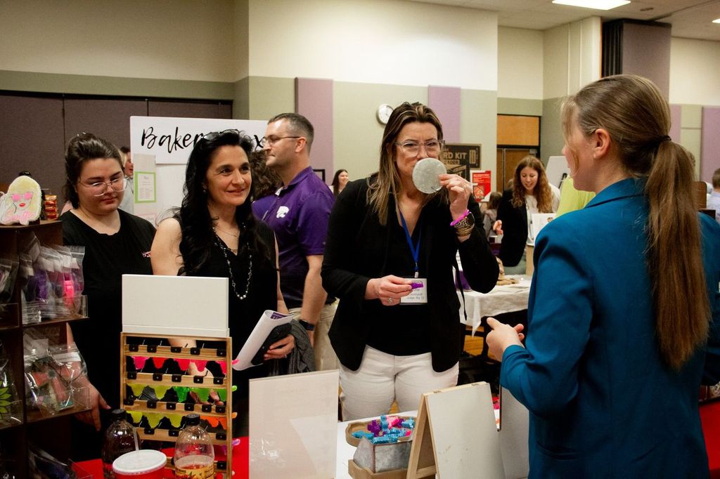 A students showcases her business to three women at the Kansas Entrepreneurship Challenge trade show. 