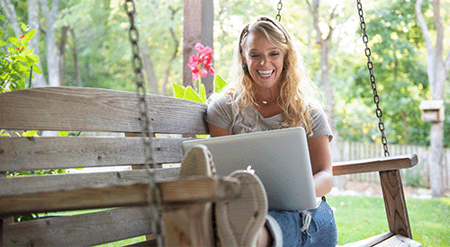 A woman learning online smiles from her porch swing