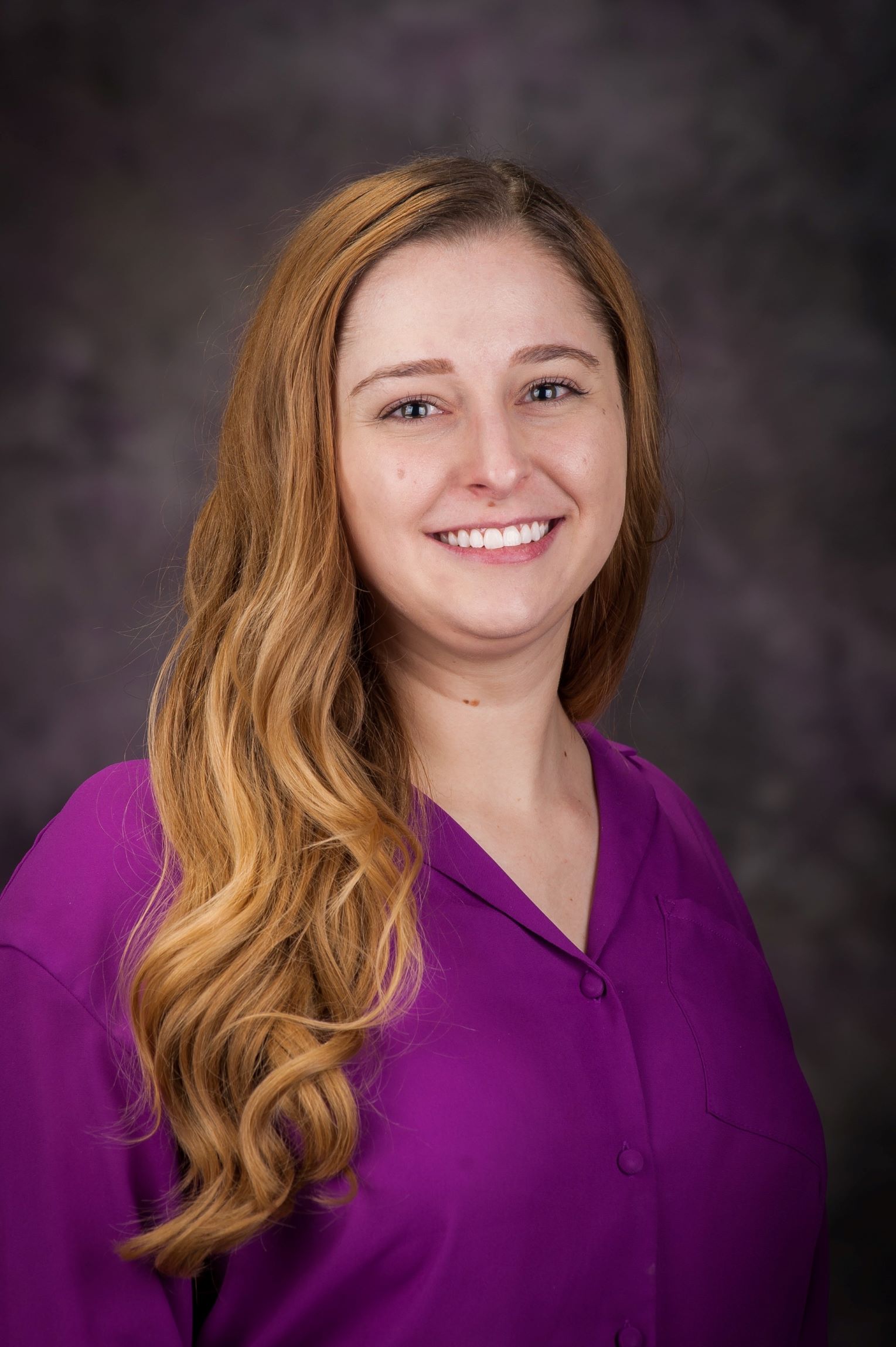 Amanda Reichenberger's headshot. She has long, caramel colored hair and is wearing a purple blouse.