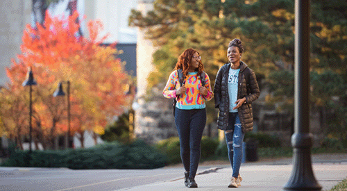 Two students walk outside of Anderson Hall on a fall day