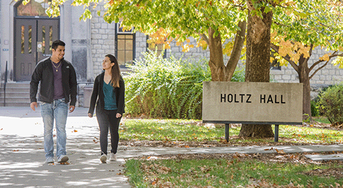 Two students pass in front of a sign that reads "Holtz Hall".