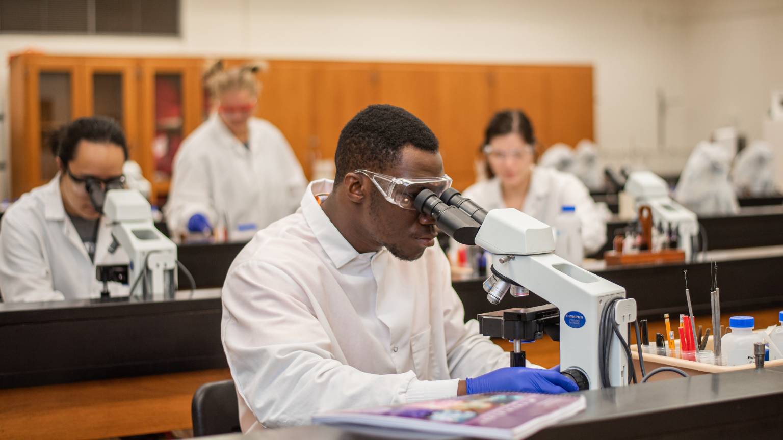 Student in a lab coat looking at scientific equipment.