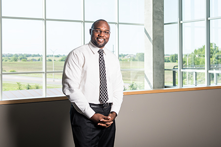 Man posing in glasses and white shirt and tie with windows behind him