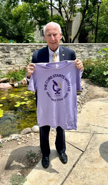 Former K-State head football coach Bill Snyder holds a "The Cure Starts With Us" T-shirt.