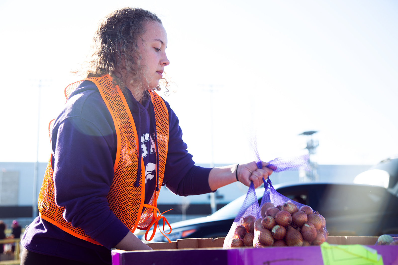 A volunteer wearing an orange safety vest lifts a bag of produce from a box