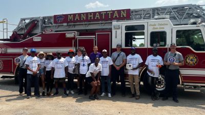 A group of volunteers stand in front of a Manhattan, KS, firetruck for a photo