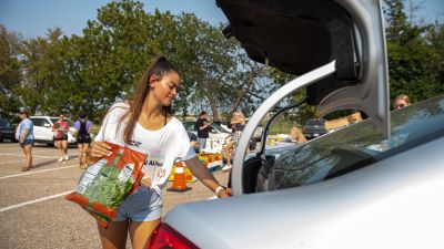 A woman places food into the trunk of a car