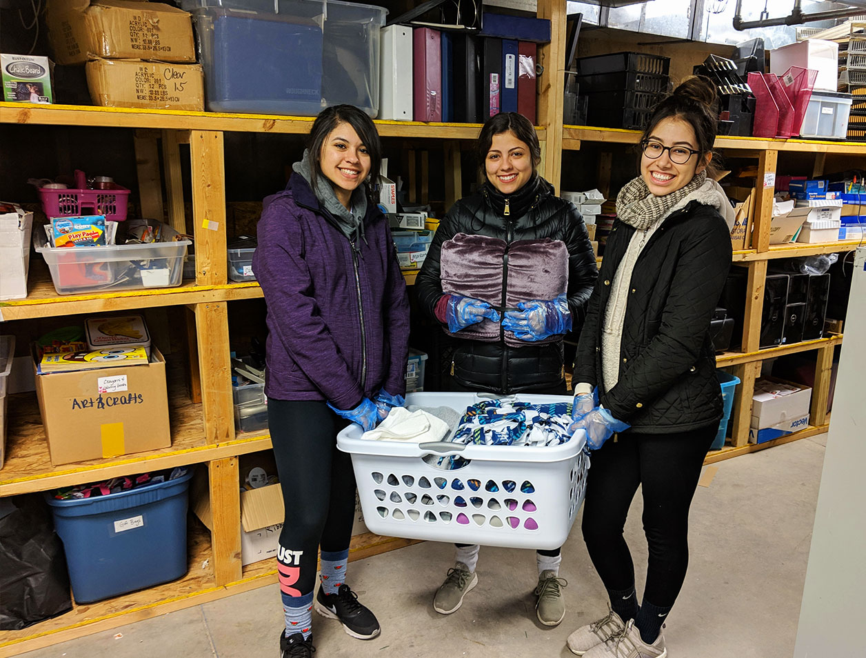 Three women hold a laundry basket full of sorted donations