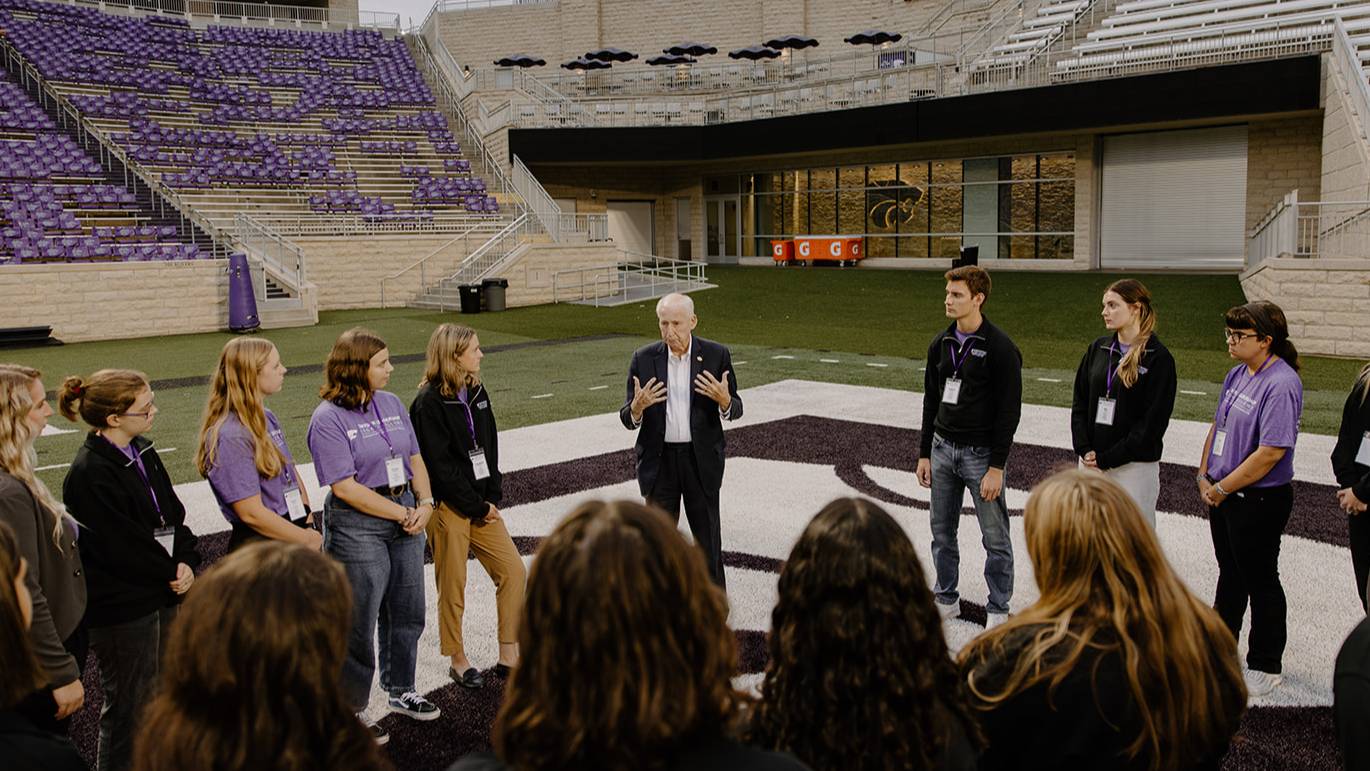 Snyder Fellows stand in a circle in Bill Snyder Family Stadium listening to Coach Snyder