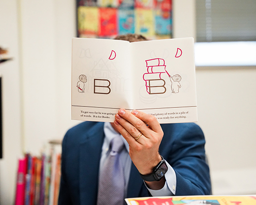 Philip Nel holds open a copy of "Harold and the Purple Crayon," which shows simple white pages with purple shapes and a bald 4-year-old child.