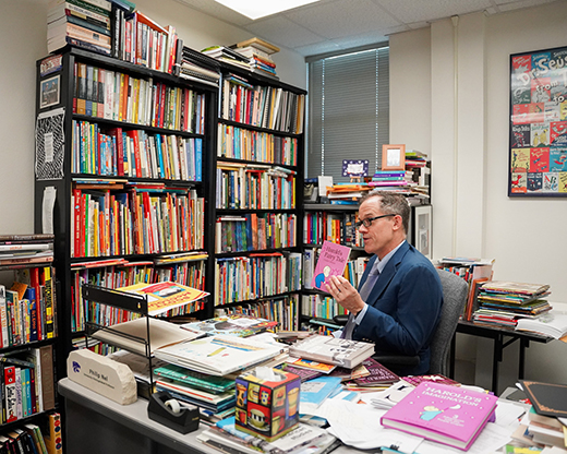 A wide shot shows almost a half-wall length of bookshelf in Philip Nel's office.