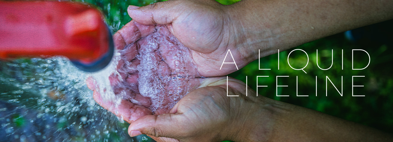 Hands outstretch under a red faucet as water pours. Overlaid text reads "A liquid lifeline."