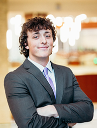 A student in a dark gray suit and purple tie.