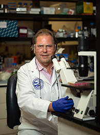 A scientist sitting a a microscrope in a white lab coat