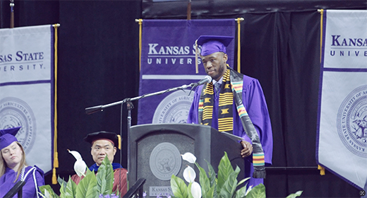 A student in purple regalia speaking at commencement