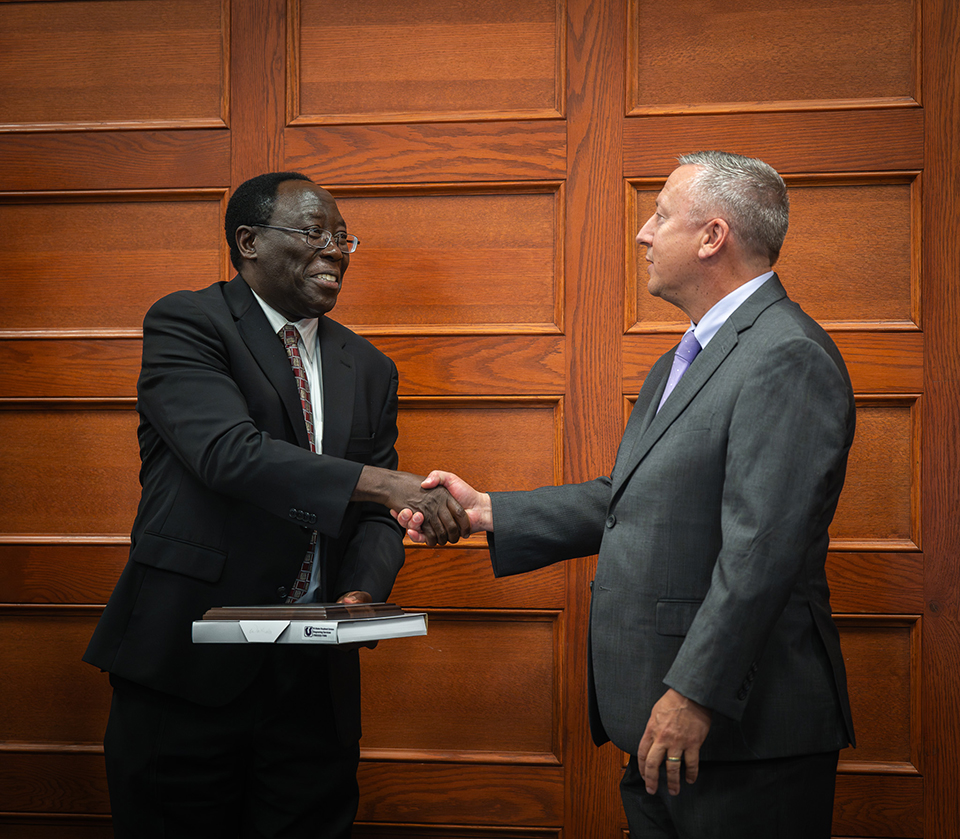 A man in a suit shakes the hand of another man as the second man presents an award to the first.