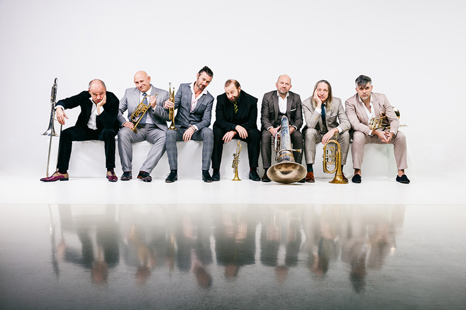 Group of musicians poses for a group photo on a white background