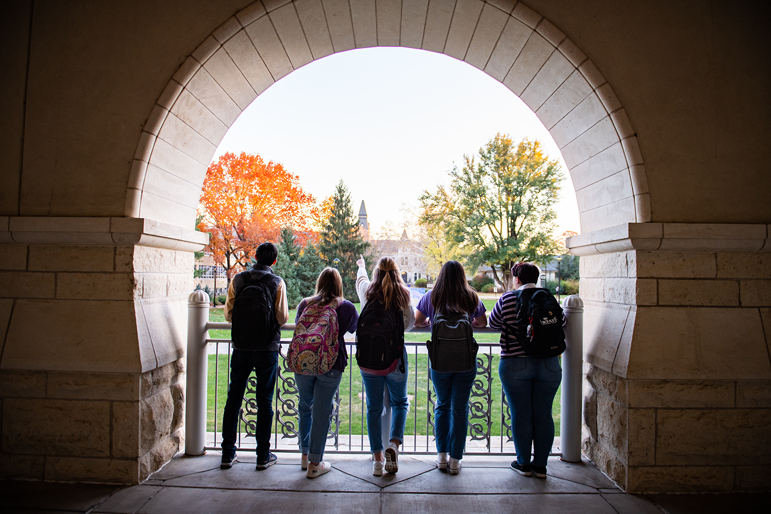 Underneath a circular opening in a limestone wall, silhouetted students look on at a bright sunny day on a university's campus.