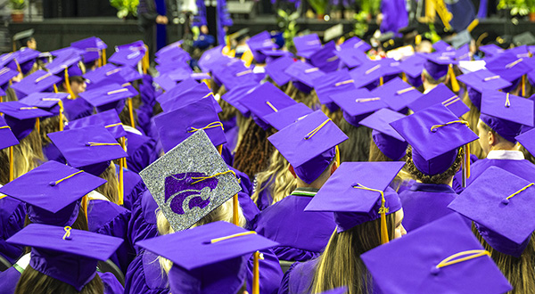 A crowd of students gathers for graduation, with purple caps and gowns.