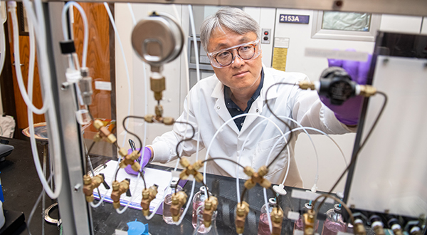 A researcher in a white lab coat adjust nozzles at a work bench.