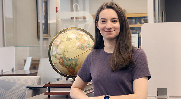 A student in a purple t-shirt poses for a portrait in front of a beige globe.