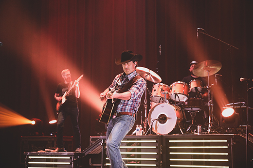 A man in a cowboy hat plays guitar onstage.