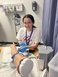 A girl practices withdrawing blood from a dummy arm.