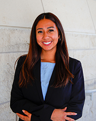 A young woman in a blazer in front of a stone wall.