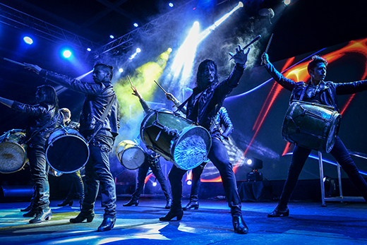 A drumline, MALEVO, on stage performing under blue lights