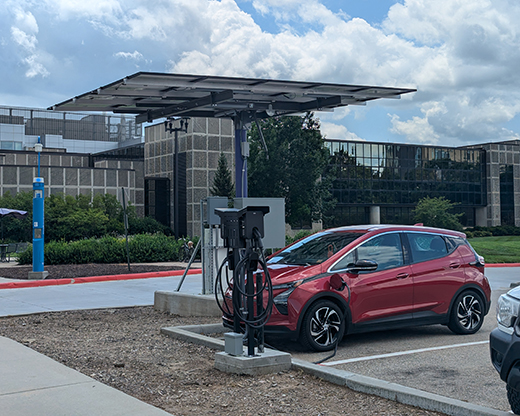 A red electric car charges during a cloudy day using the off-grid, solar powered electric vehicle charger designed and partially installed by K-State engineering students.