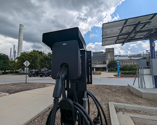 A black device on a pedestal has an electric car charger plugged into it in standby mode.