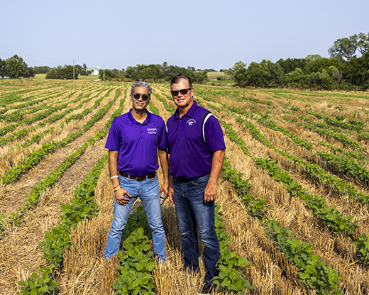 Two men — one a farmer and the other a K-State agricultural engineer — in purple polos stand in a field.