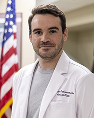 Britton Scheuermann, wearing a white lab coat, poses for a photo.