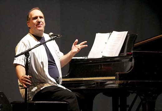 A man sitting at a piano talking to a crowd