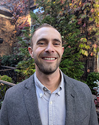 A man smiling in front of greenery