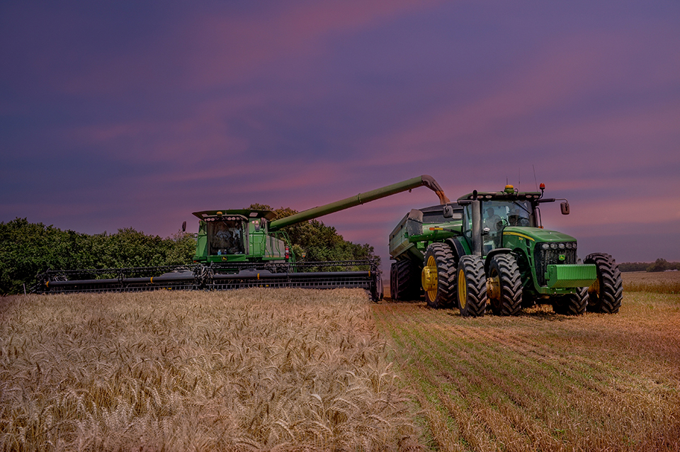 Farm equipment in a field with a purple sunset