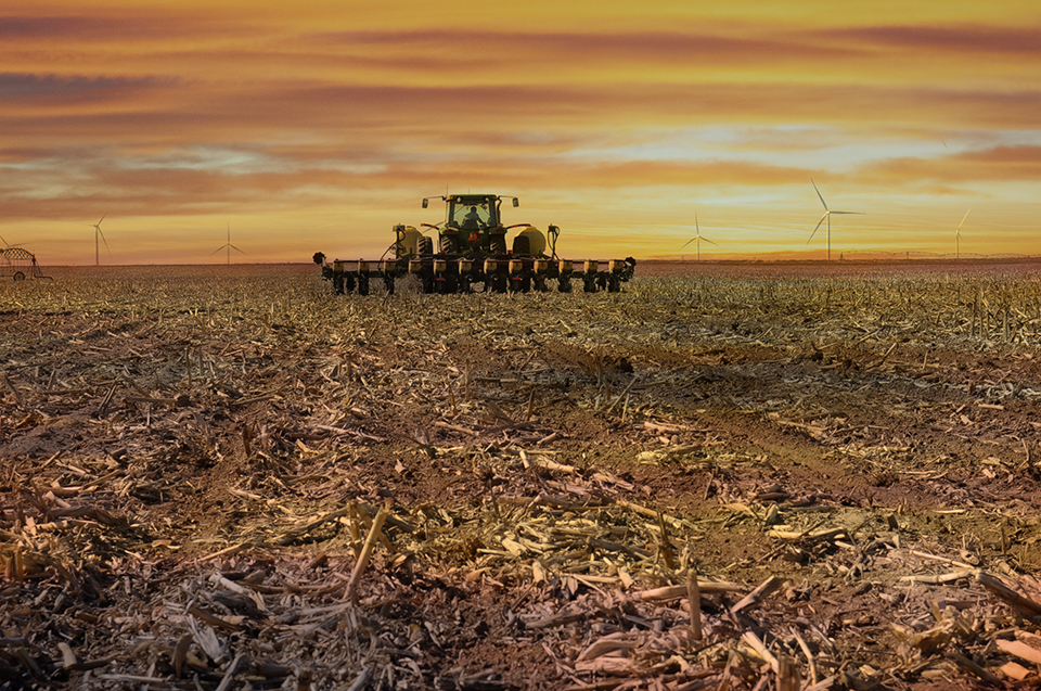 Farm equipment in a field with a yellow and orange sky