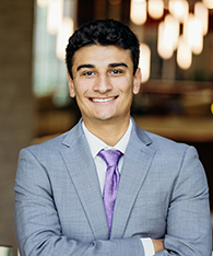 A young man in a light gray suit with a purple tie.