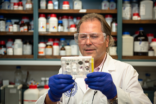 A man in a white lab coat and safety glasses looking at a sample