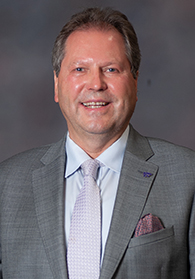 A man in a gray suit smiling in a portrait photo.