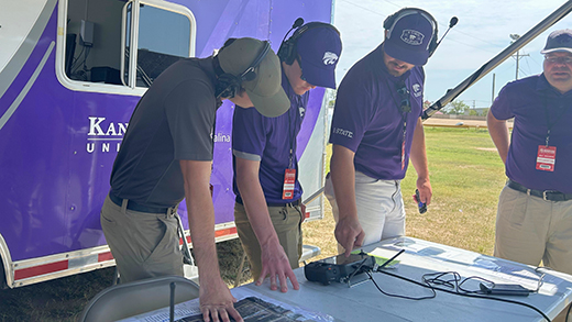 a-group-of-men-in-headsets-gathered-around-a-monitor