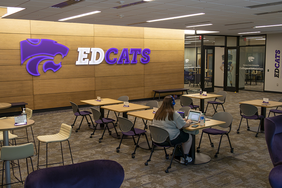 A student studies inside the spacious EdCat Lobby as part of the renovations to Bluemont Hall, while a lit-up "EdCats" sign hangs on the wall behind.