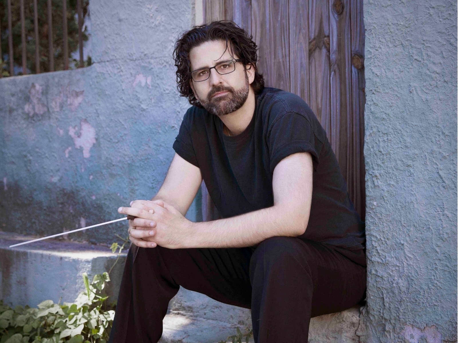 amit peled sitting on a doorstep holding a conductor's baton