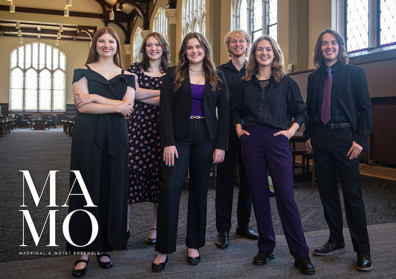Four singers in black, stand behind music stands.