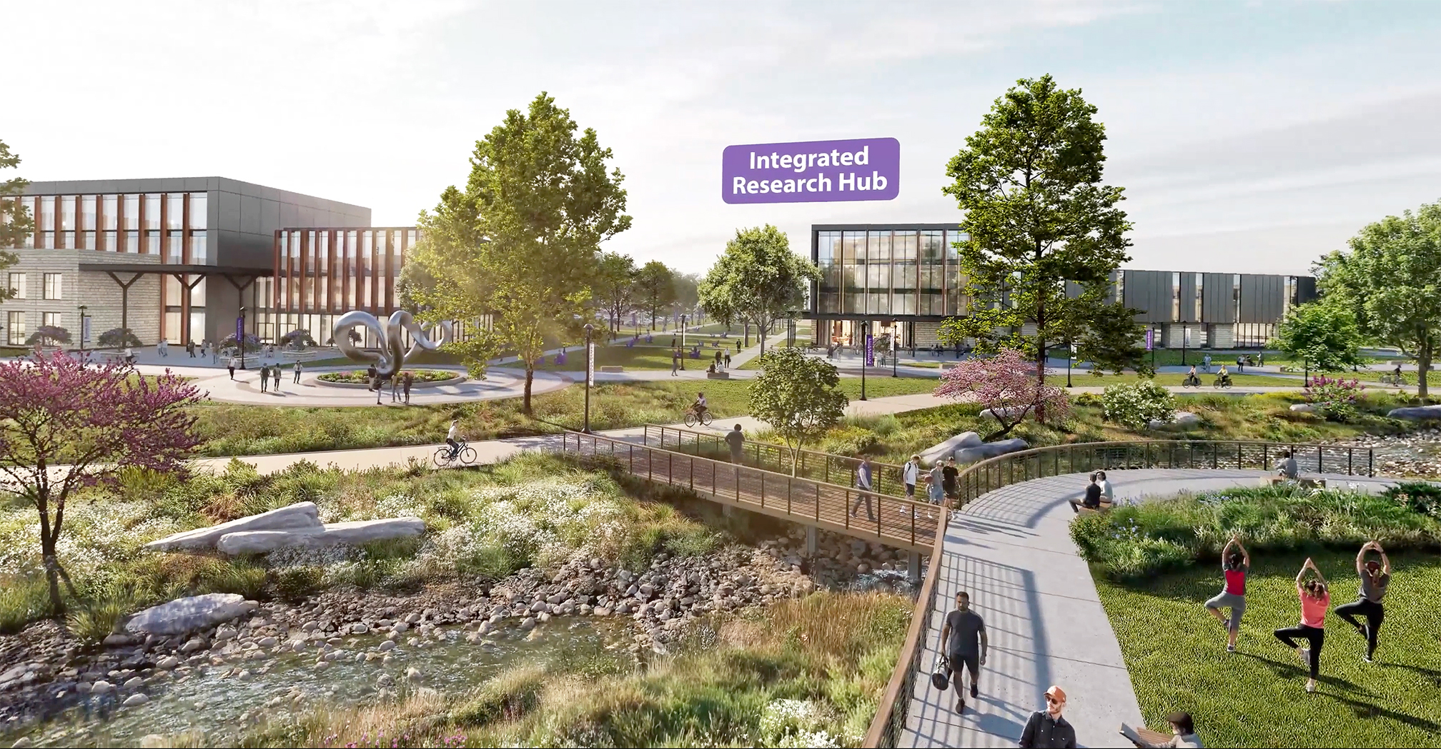 A rendering of a revitalized campus: On the far left, a building of lilmestone with many windows sits behind a circular walkway with a silver geometric sculpture in the middle. Trees and a grassy area with sidewalks are next to the building. A creek with rocks and water flows through teh area, with a brown bridge over the top connecting walkways. In the back right of the rendering, a tall building with square windows and a dark exterior is labled with a purple rectangle "Integrated Research Hub," identifying a newly proposed initiative. At the far right of the rendering, three people are practicing yoga on a grassy area.