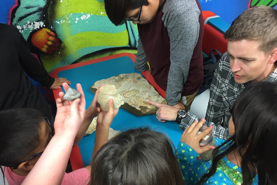 Matthew Kirk teaches Kickapoo children about geology using several rocks at a play table.
