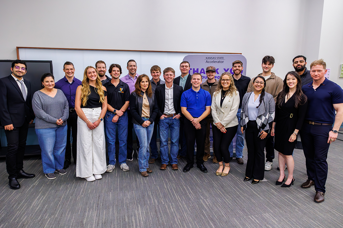 A group of 20 entrepreneurs in professional attire stand inside a room on gray carpet.