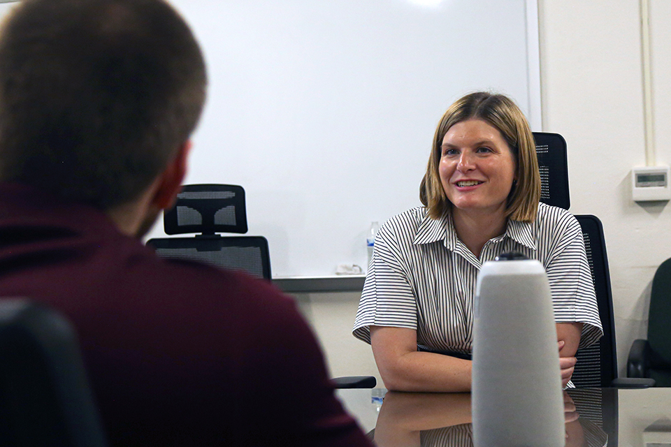 A college professor sits and looks at a presentation off-screen next to one of her students.