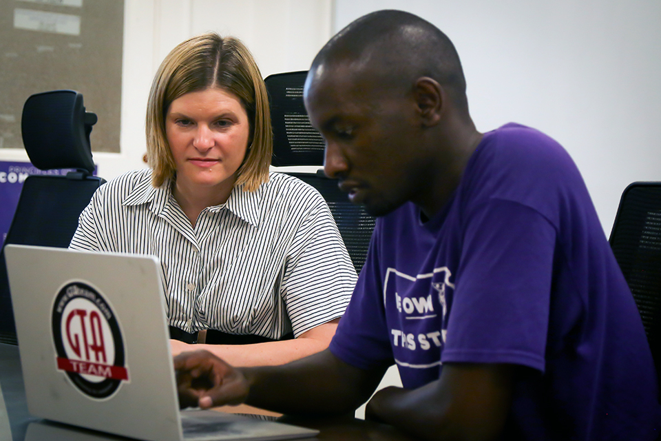 College professor Amanda Gaulke looks over a student's shoulder at a table.